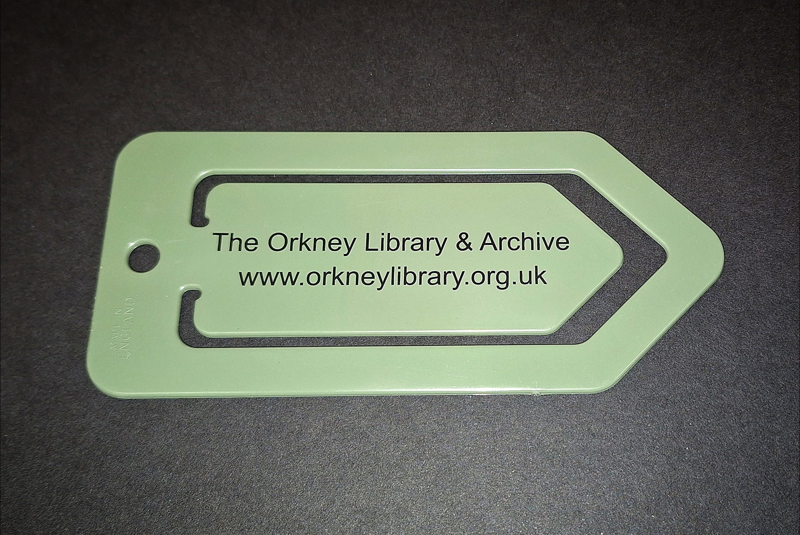 A green plastic bookmark with an arrow shape and a small circular hole on one end. It features the text "The Orkney Library & Archive" and "www.orkneylibrary.org.uk" printed in black.